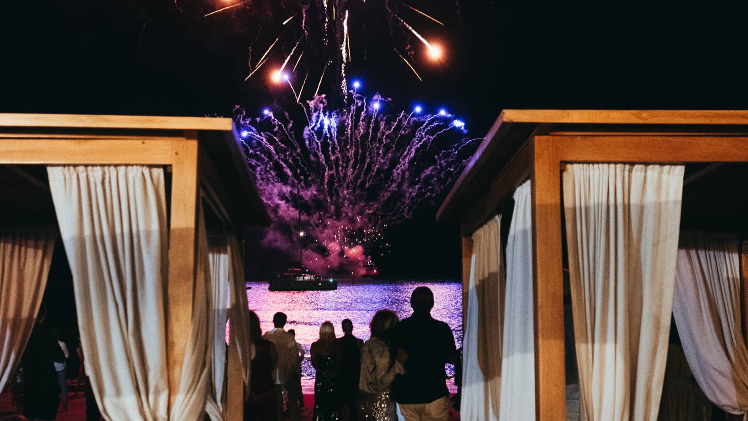 Fireworks light up the night sky over rows of beach cabanas