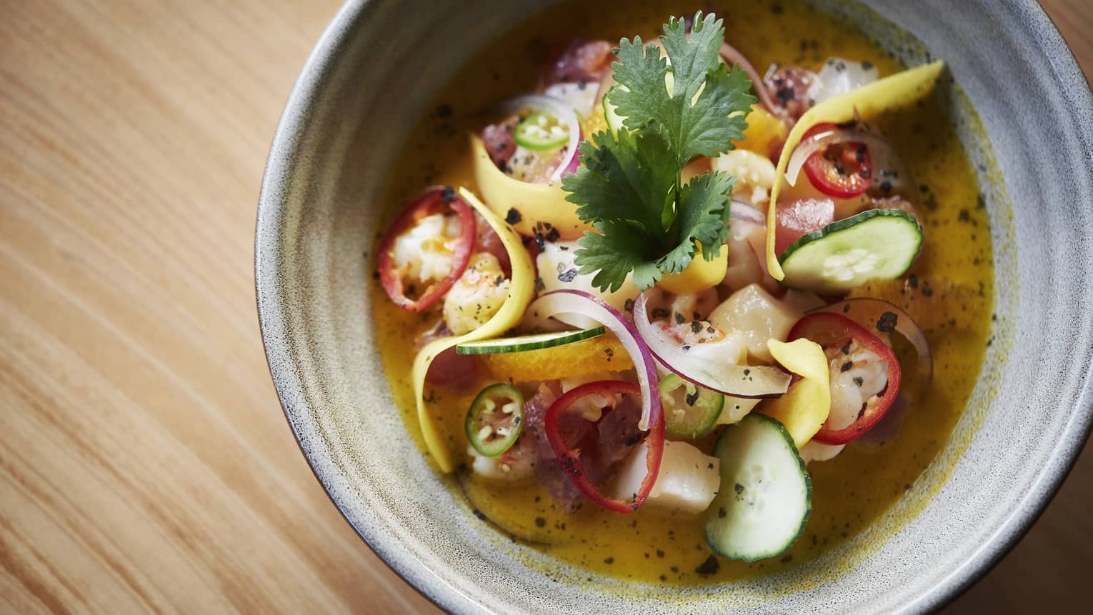 A gray ceramic bowl of a vegetable, curry soup garnished with cilantro and jalapenos 