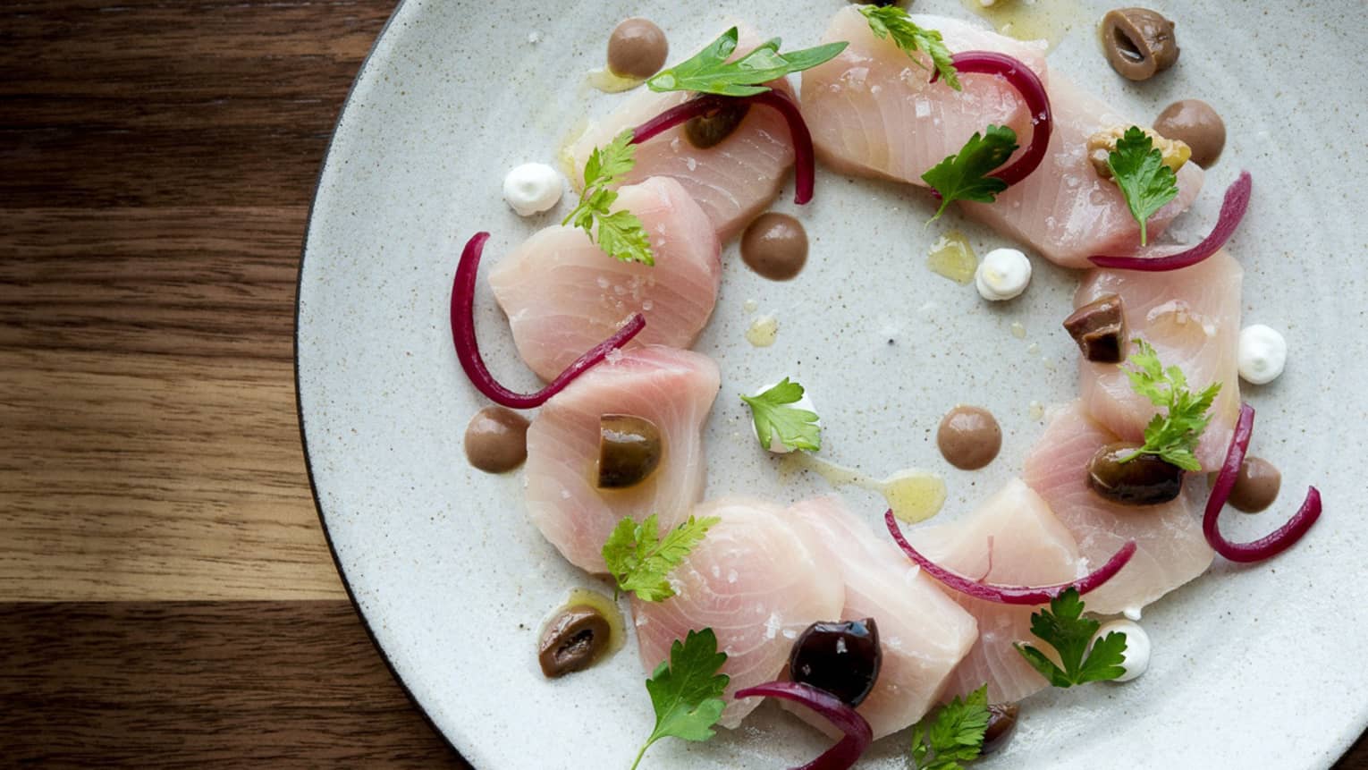 Hamachi Crudo slices of raw fish arranged in circle on plate with garnish