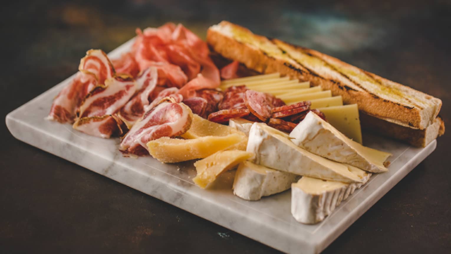 Kobe bresaola, cured duck breast, Camembert and aged cheddar on a marble cutting board. 