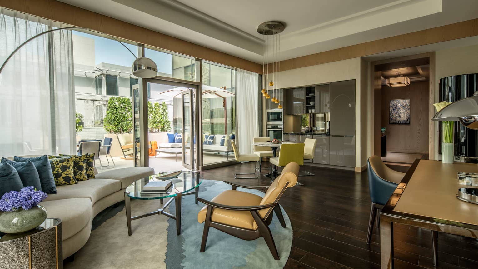 Terrace Suite bright living room curved sofa, accent pillows, leather armchair, floor-to-ceiling windows, dining tables