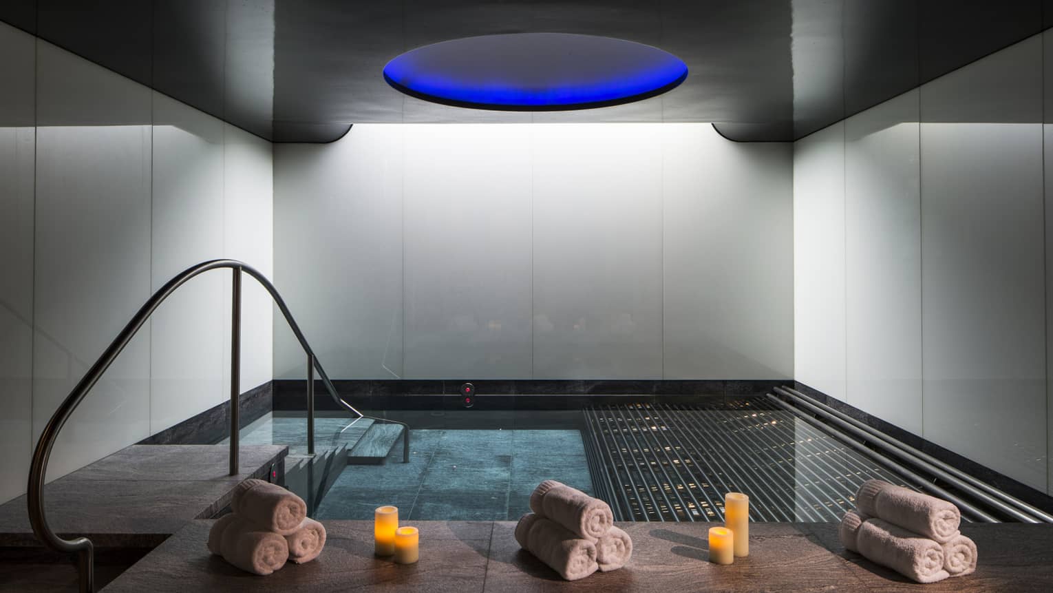 Rolled white towels, candles on spa vitality pool ledge under blue dome ceiling