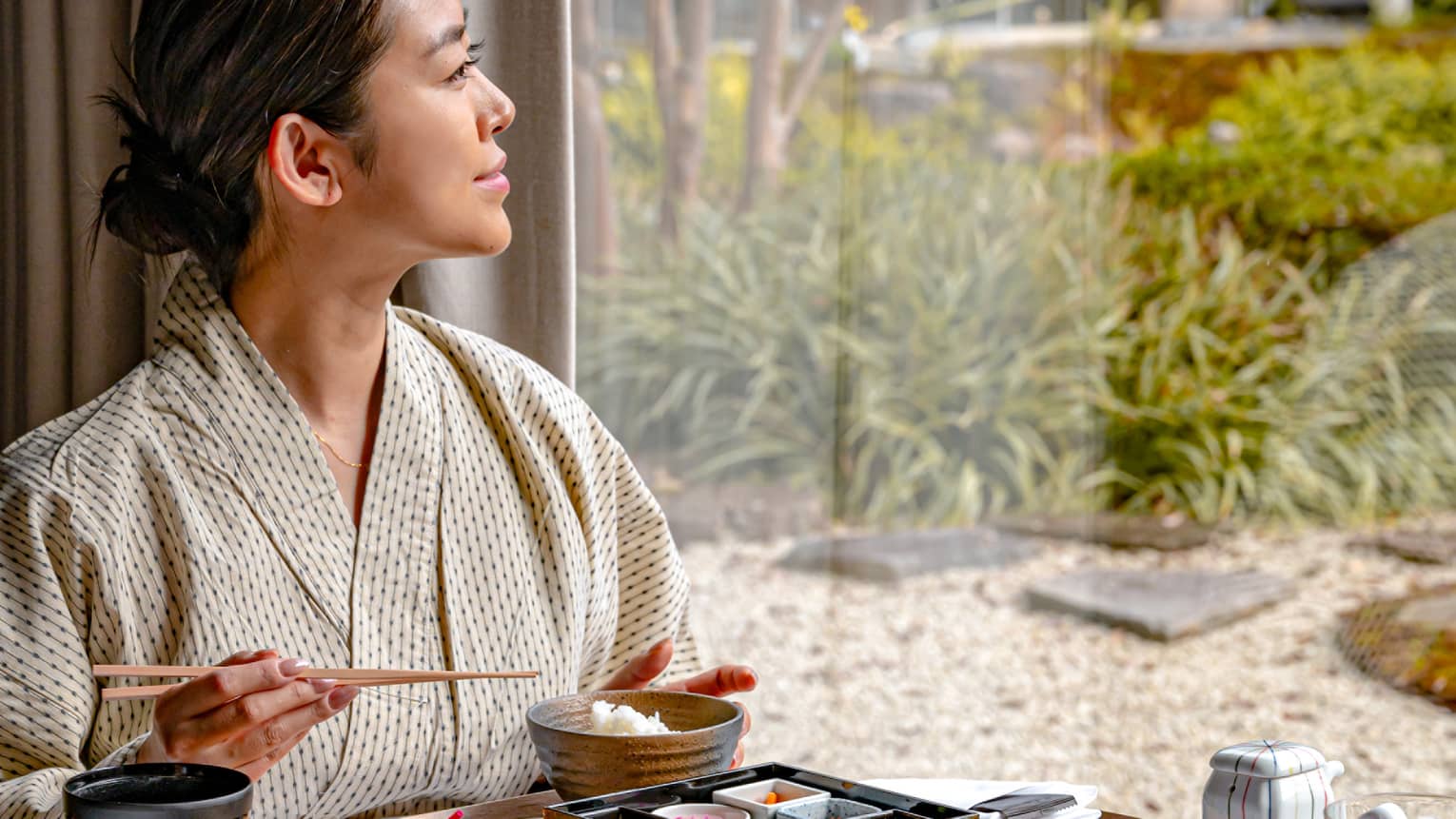 Woman eats breakfast in luxury hotel looking out window to garden