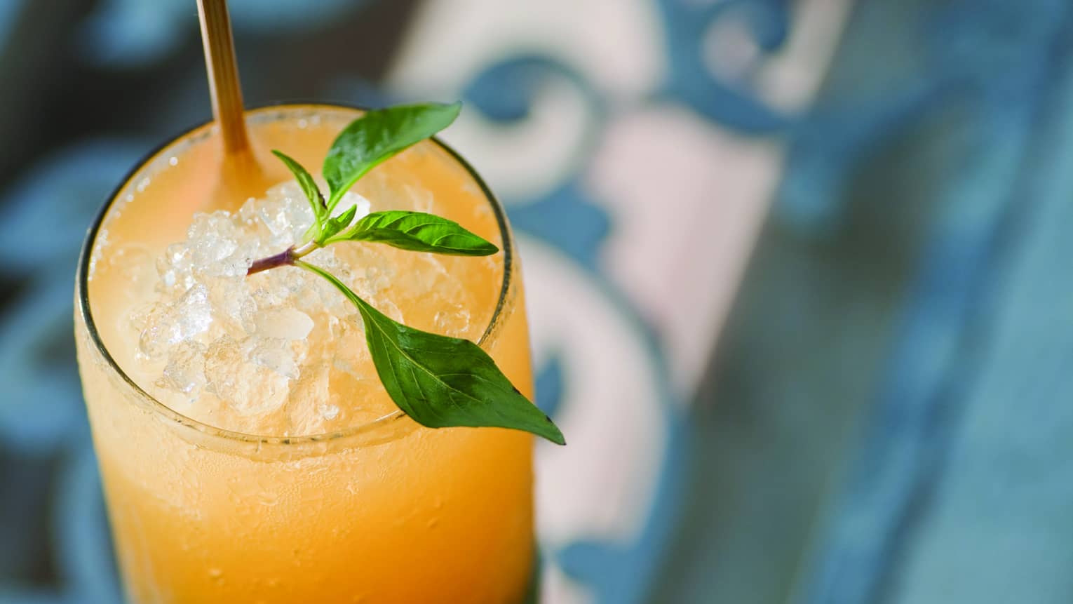 Bright yellow cocktail in tall glass with crushed ice, garnished with sprig of Thai basil