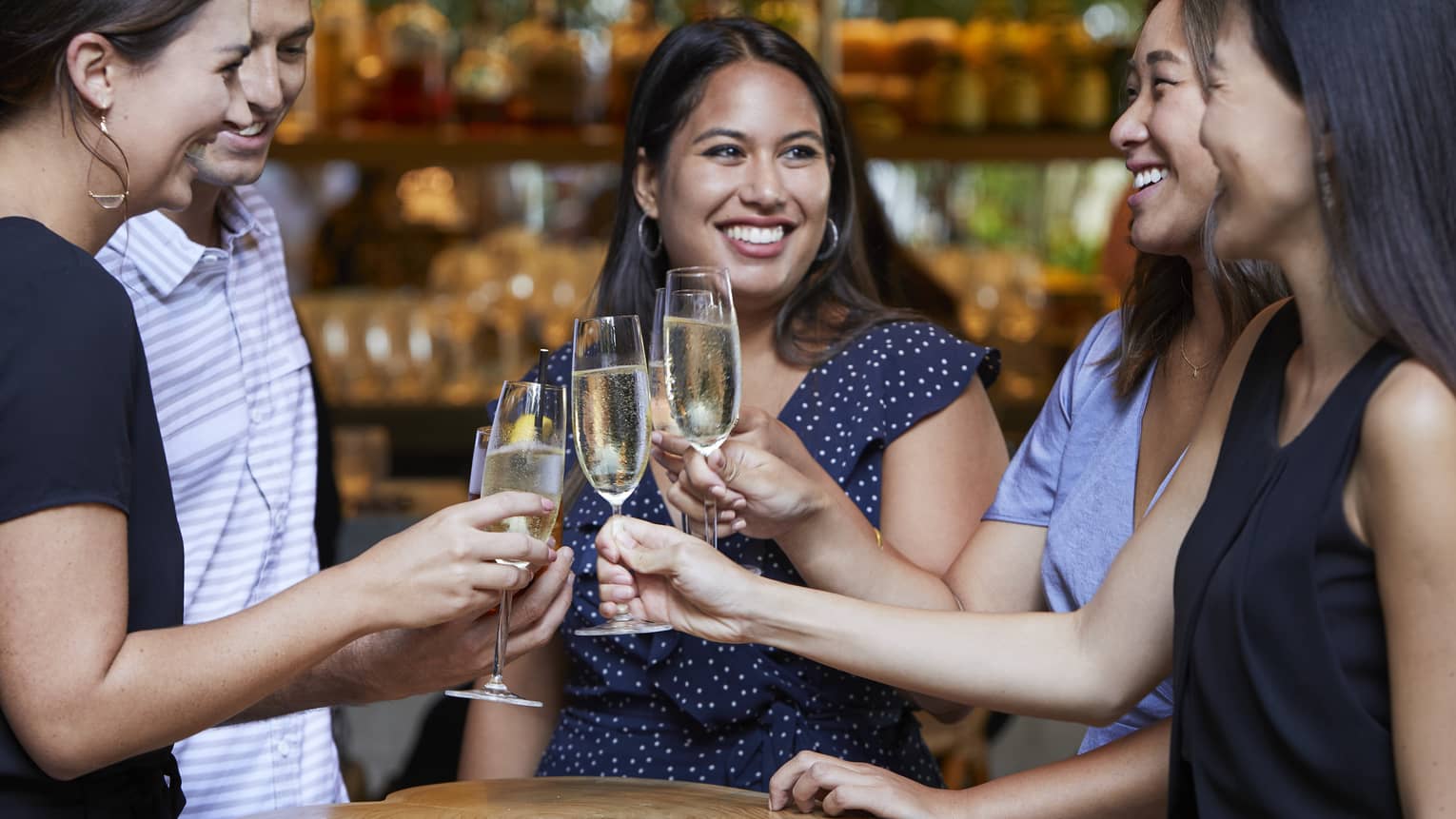 Group of friends share Champagne toast over rustic wood cocktail table