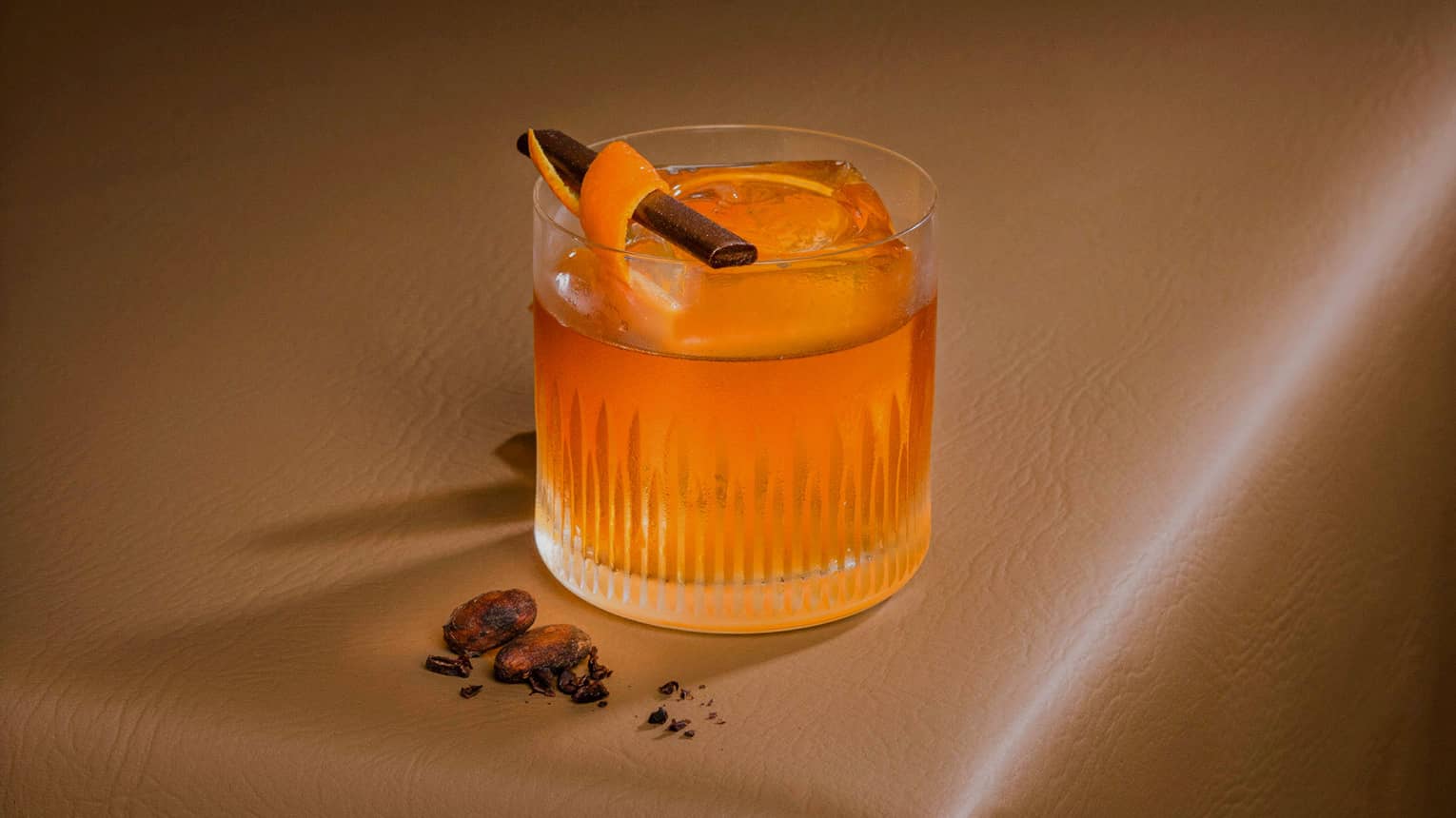 Segua's Old Fashioned cocktail in a lowball glass garnished with an orange peel and cinnamon stick sits on a brown leather tabletop