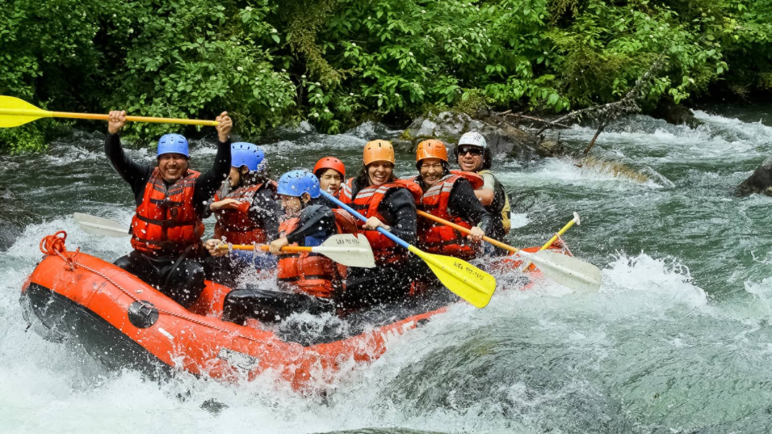 Smiling family wearing life jackets, helmets on white water raft on river rapids