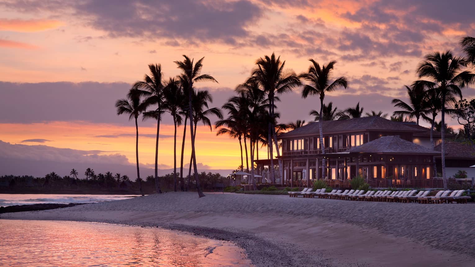 Silhouettes of Four Seasons Resort Hualalai building, tall palm trees on beach at sunset