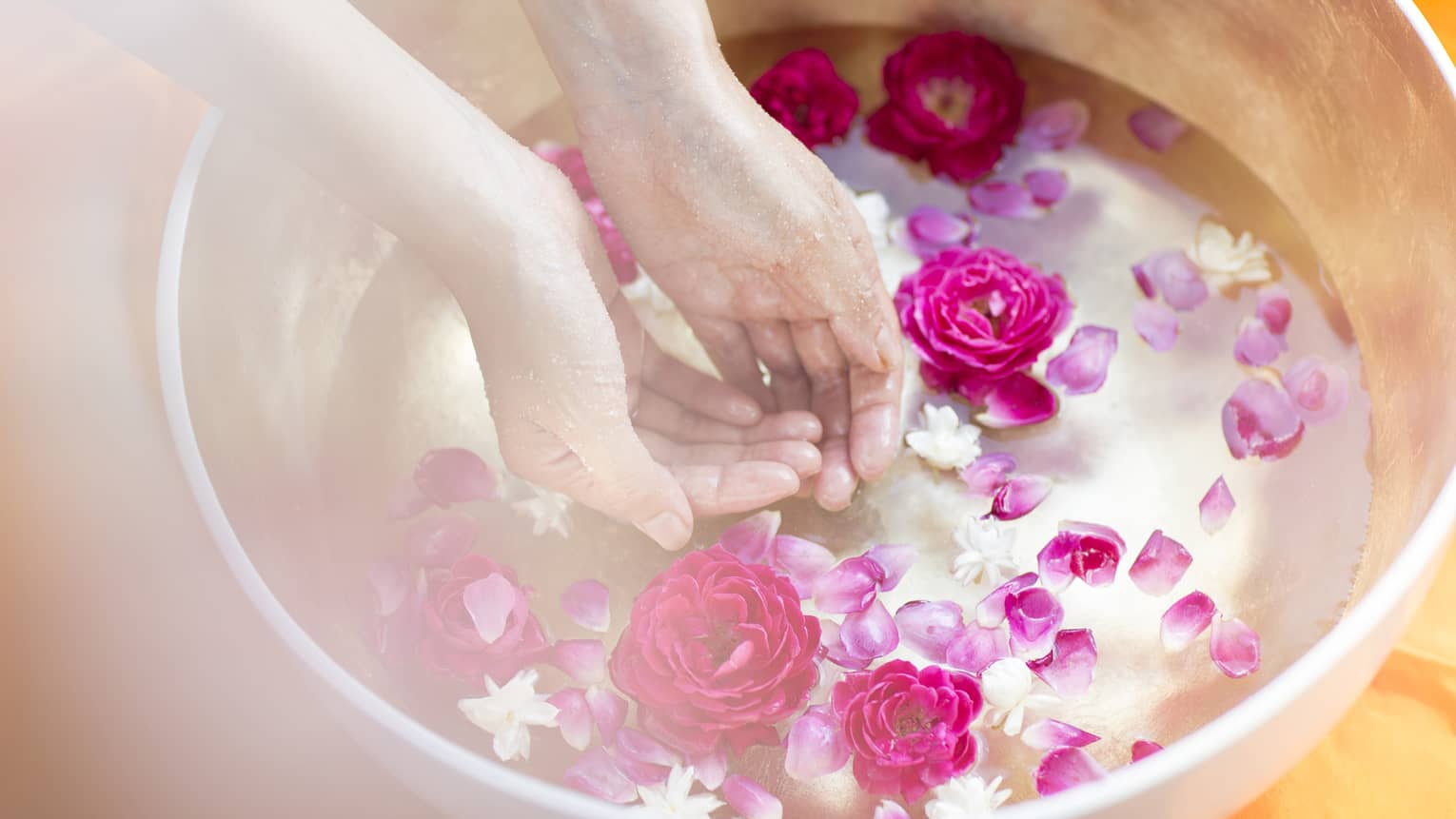 Woman's hands in bowl of water filled with pink and white flowers, petals