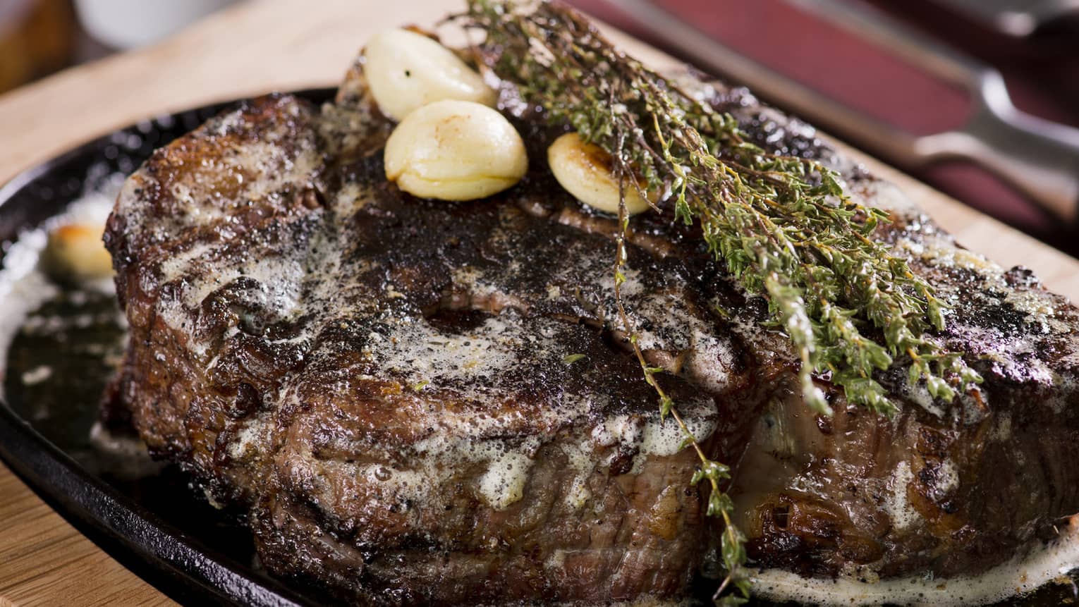 A large steak on a stone and wood tray.