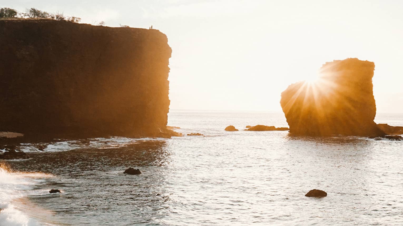 Sun sets over large rocks in lagoon