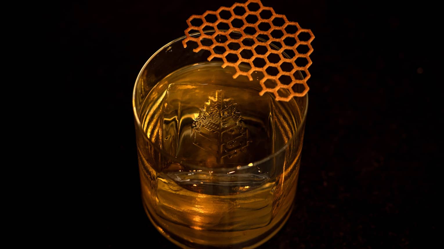 A clear tumbler contains a golden-hued cocktail, ice and garnish