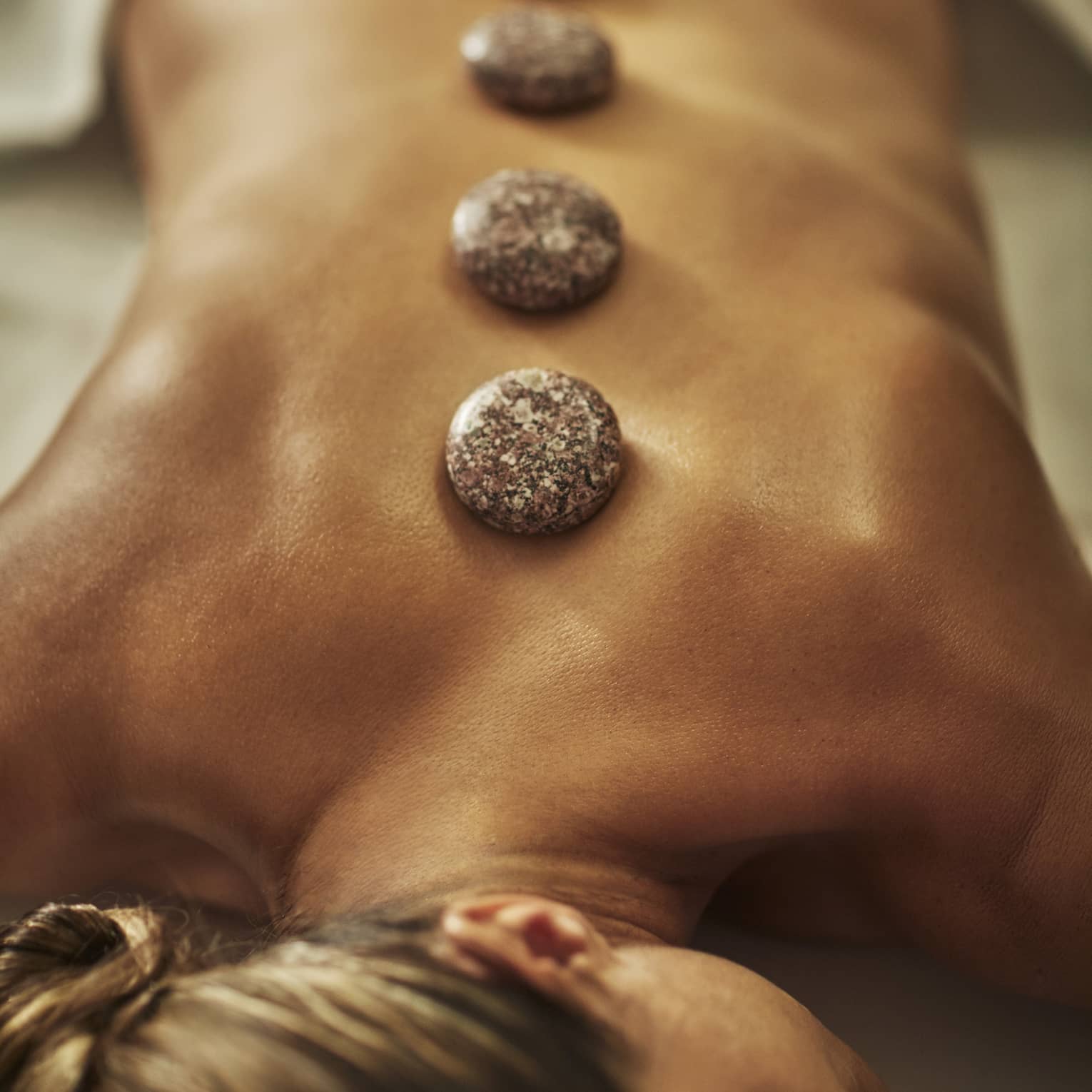 A woman lies on a spa table with four hot stones laid on her back