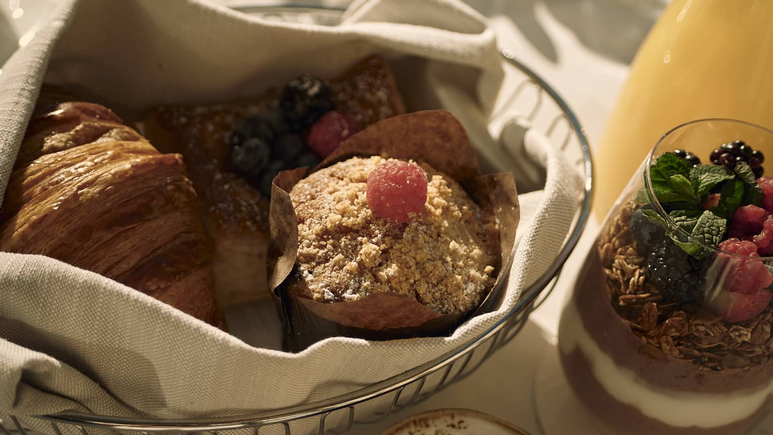 Various pastries in a basket with a yogurt parfait beside it