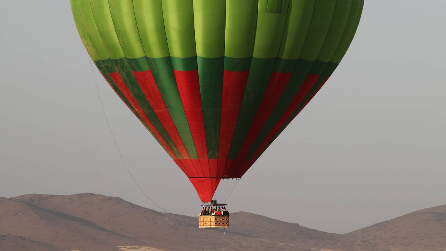 Man stands in field under large green and red hot air balloon 