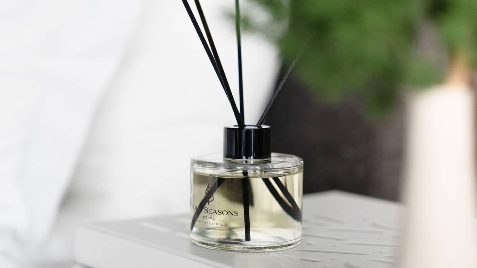 Four Seasons Hotel Tokyo at Otemachi diffuser in cylindrical glass bottle with black reed sticks on stack of white books on nightstand