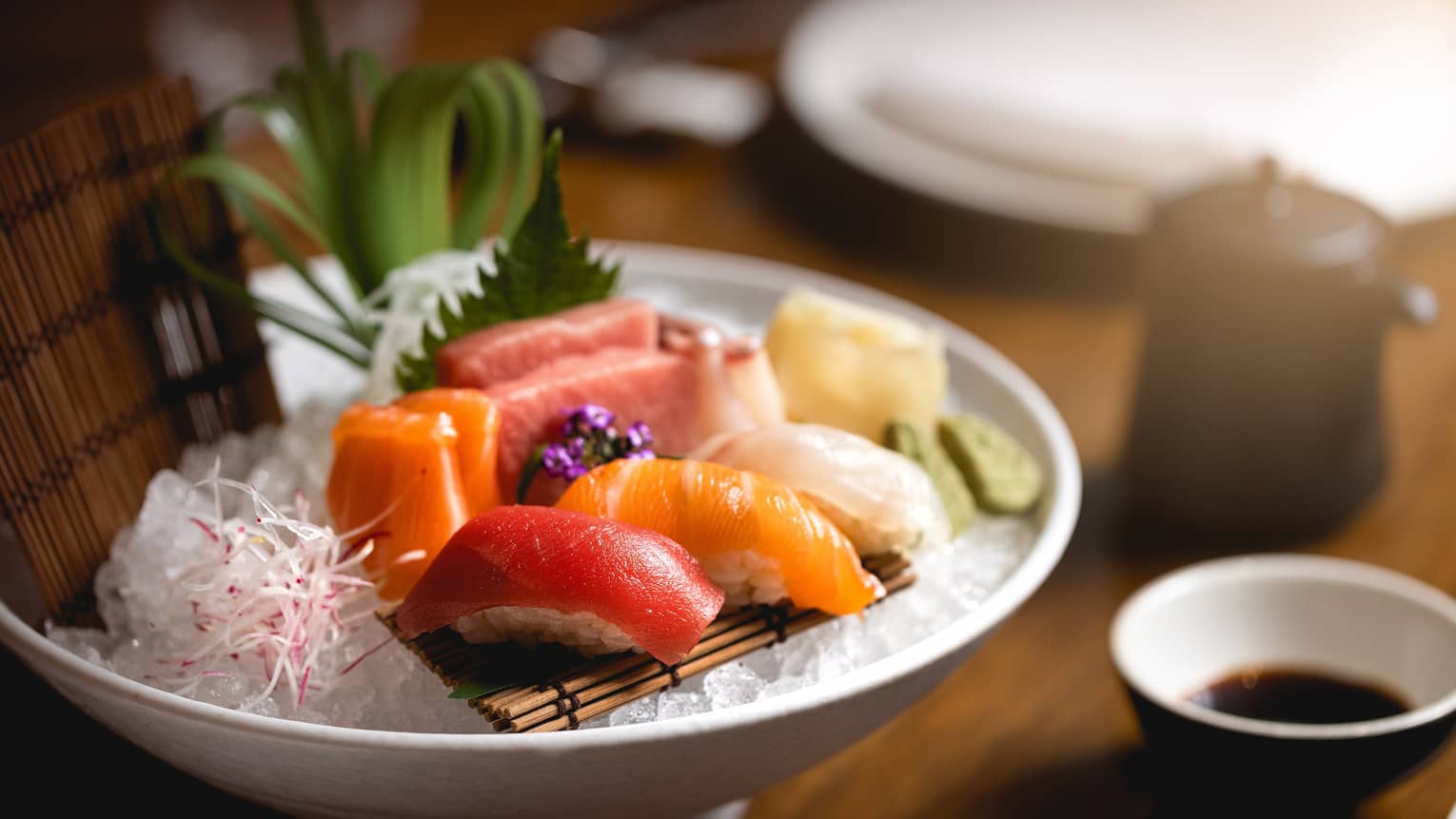 Colourful sashimi and nigiri on bamboo mat atop crushed ice in white bowl