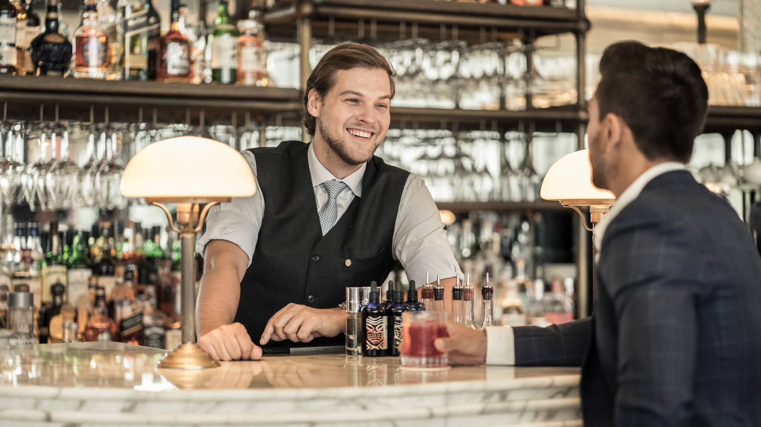 A bartender smiles at a guest enjoying a cocktail.