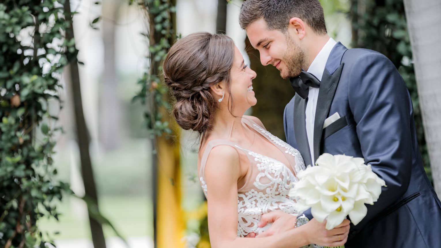 Smiling groom and bride with white wedding dress, bouquet embrace