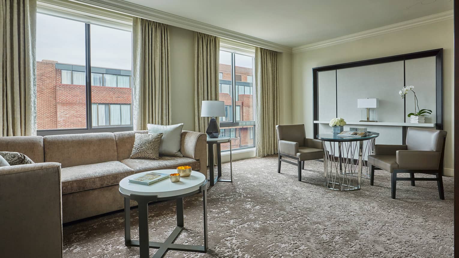 Premier Suite grey L-shaped sofa, small round white table, cafe-style dining table, large windows