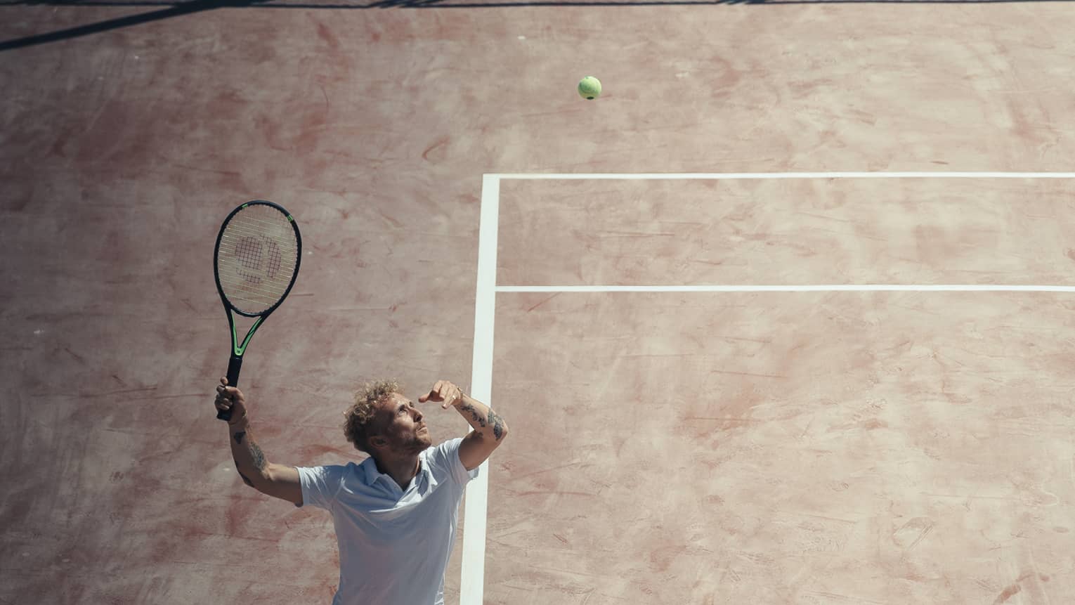 Man in white outfit playing tennis on reddish clay court