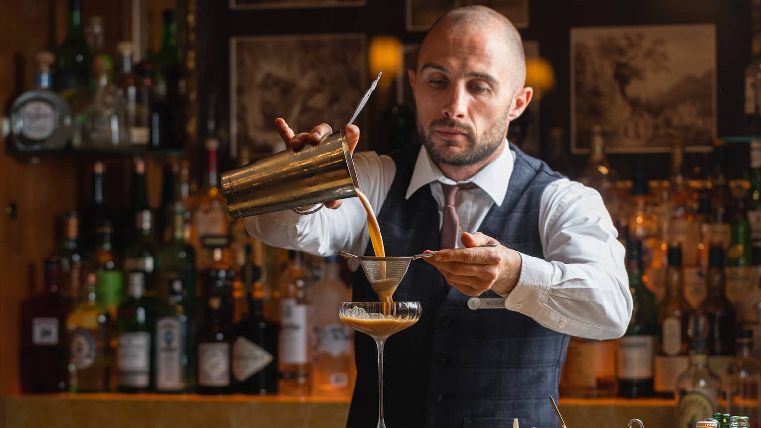 A bartender pouring a cocktail into a glass.