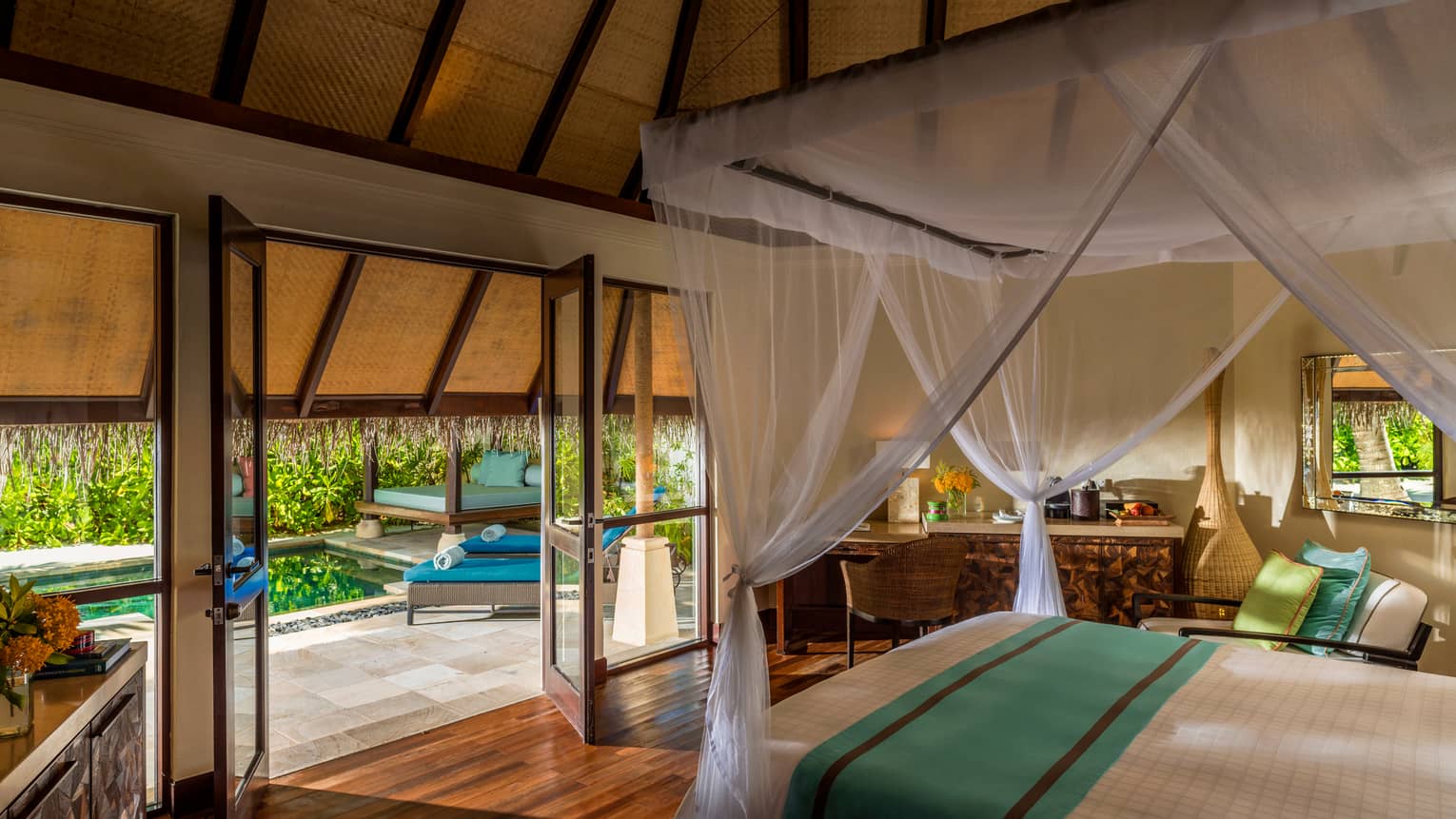 Traditional beach pavilion suite with canopy bed and open-air doors and windows leading to patio