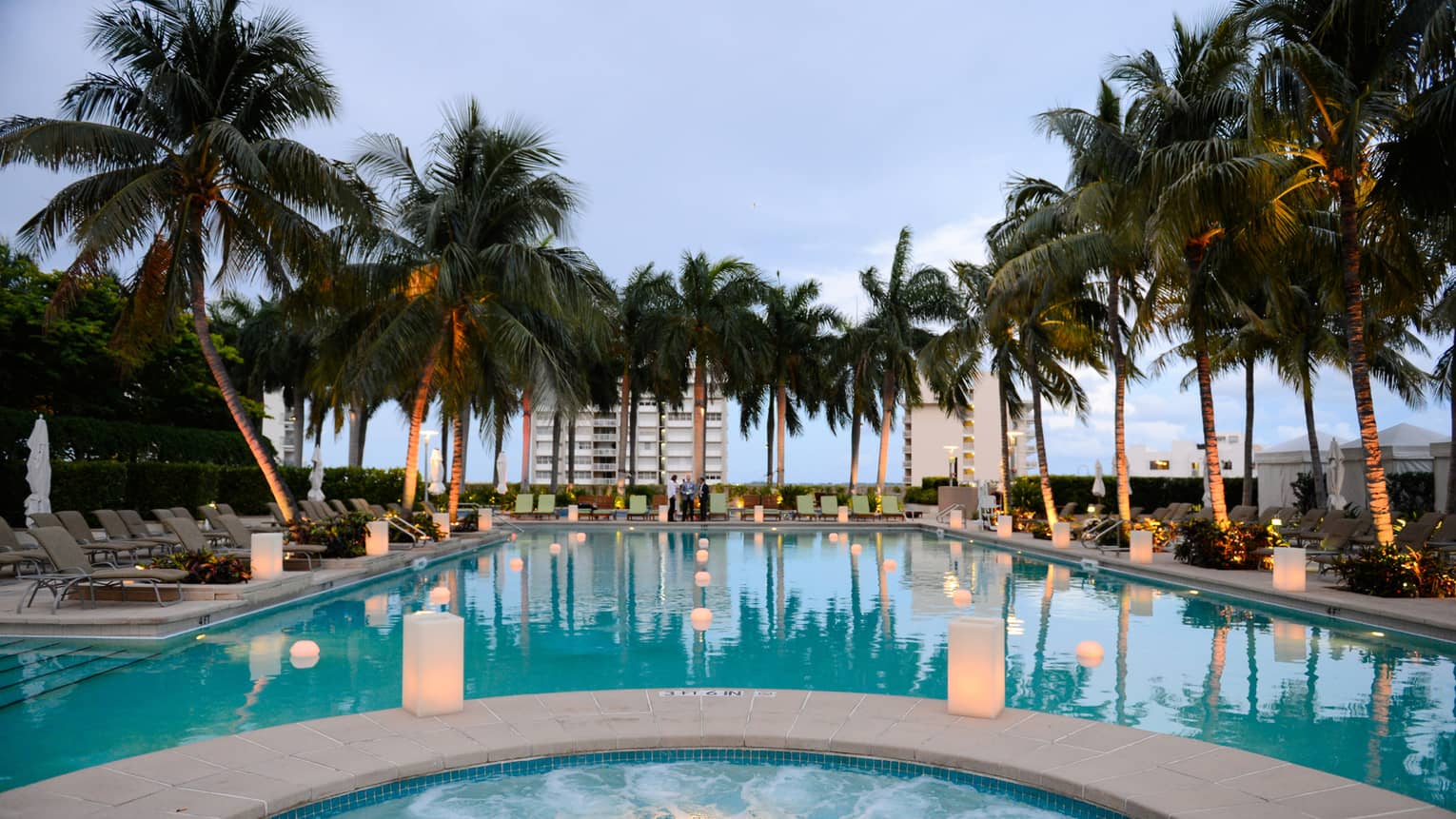 White lanterns glow along outdoor pool lined with palm trees