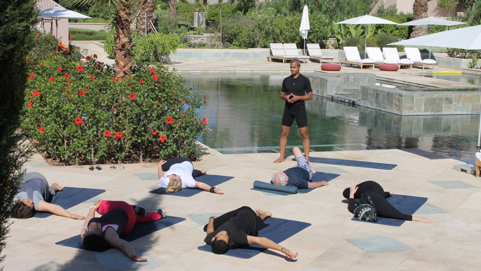 Fitness class on patio, instructor stands over people stretching on yoga mats