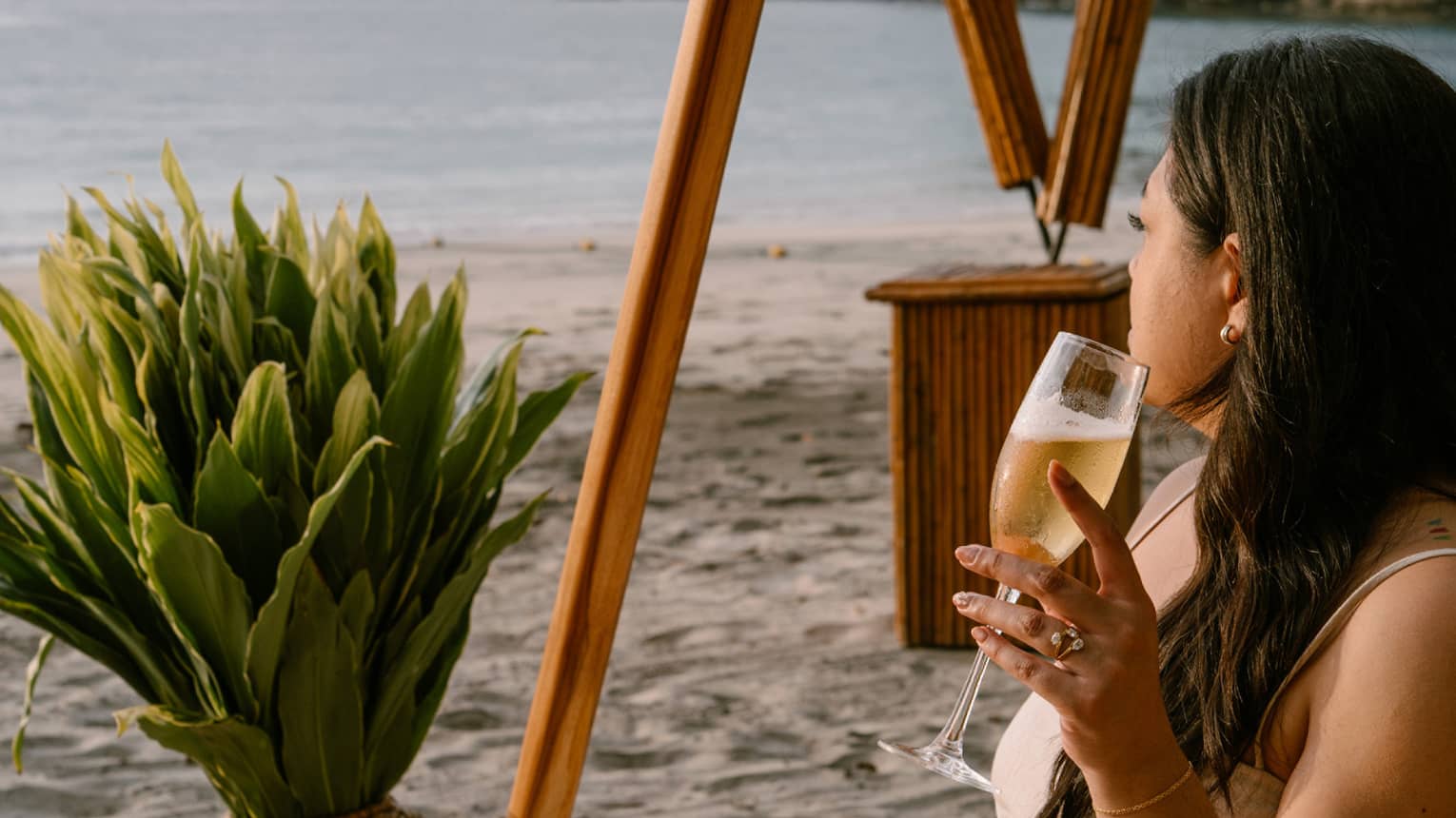 Guest sits on an acapulco chair on the beach while looking out onto the ocean with a beverage in hand