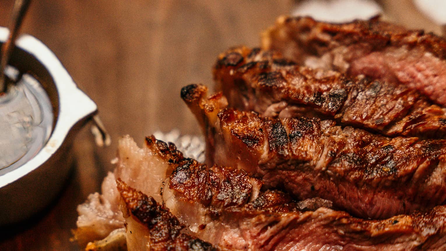 Close up of rack of ribs on a wooden board next to a small silver bowl of sauce