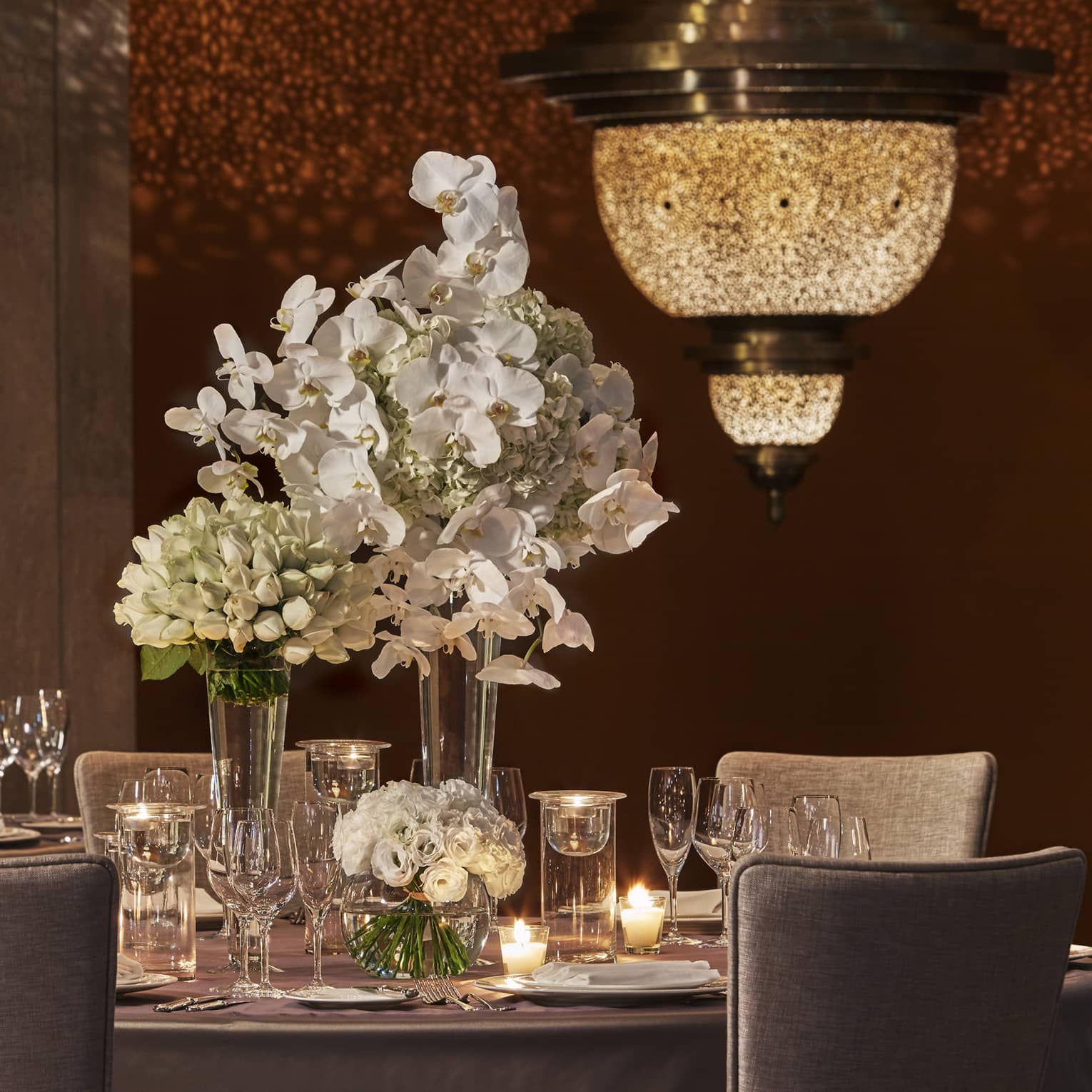 Moroccan chandelier casts shadows on wall by dining table with white flowers, candles