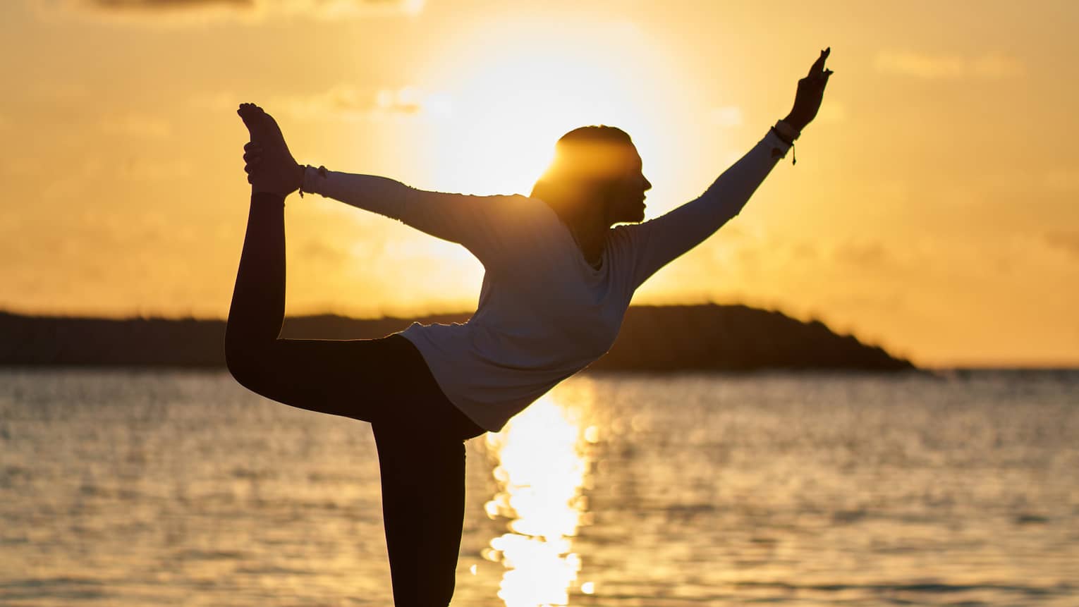 Woman doing yoga pose on beach at sunset