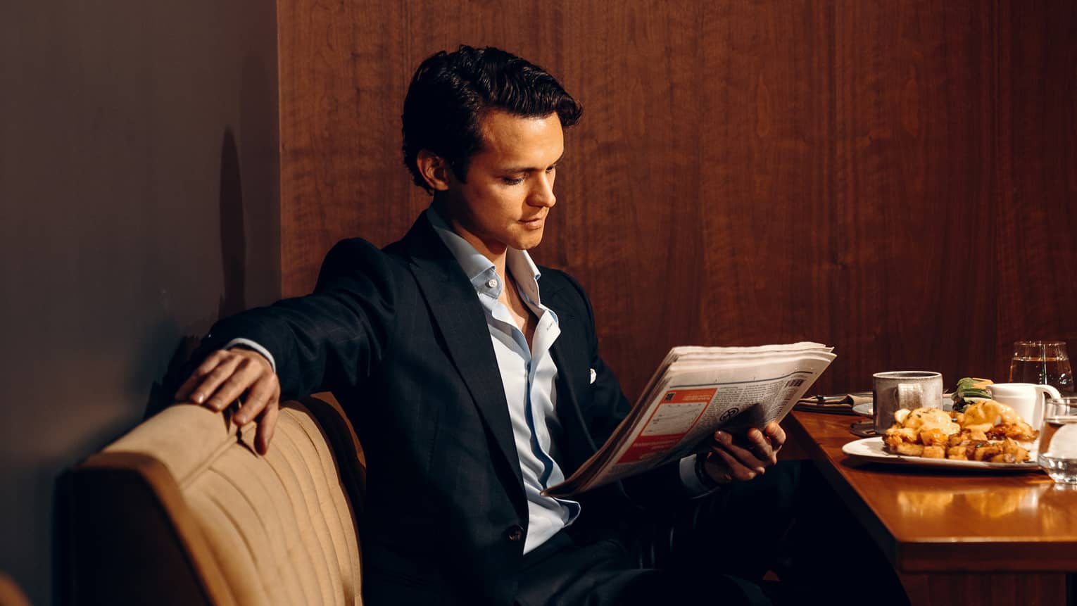 Person reading a newspaper while sitting at a dining table.