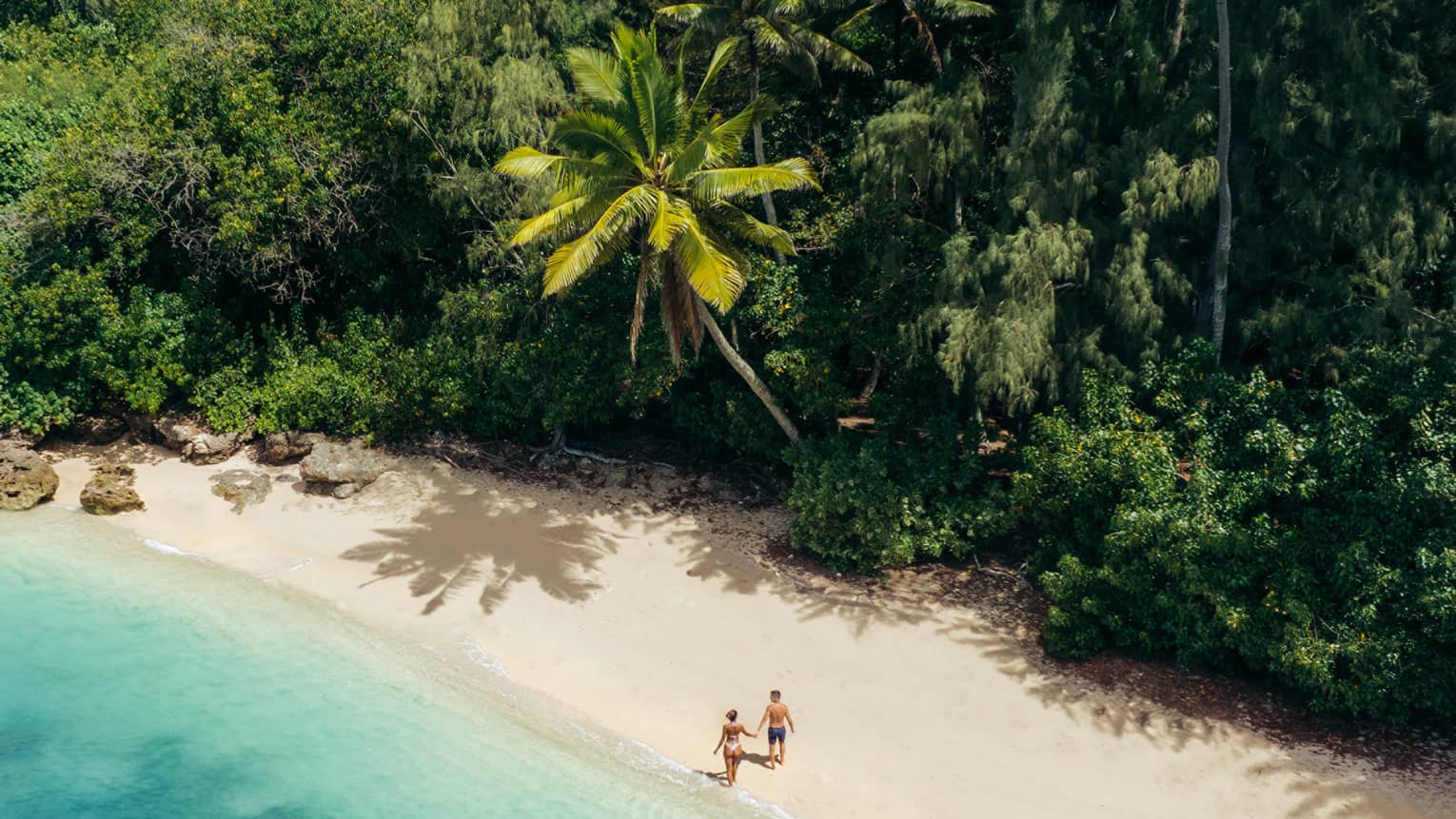 Two people walking on private beach with tropical trees and turquoise water