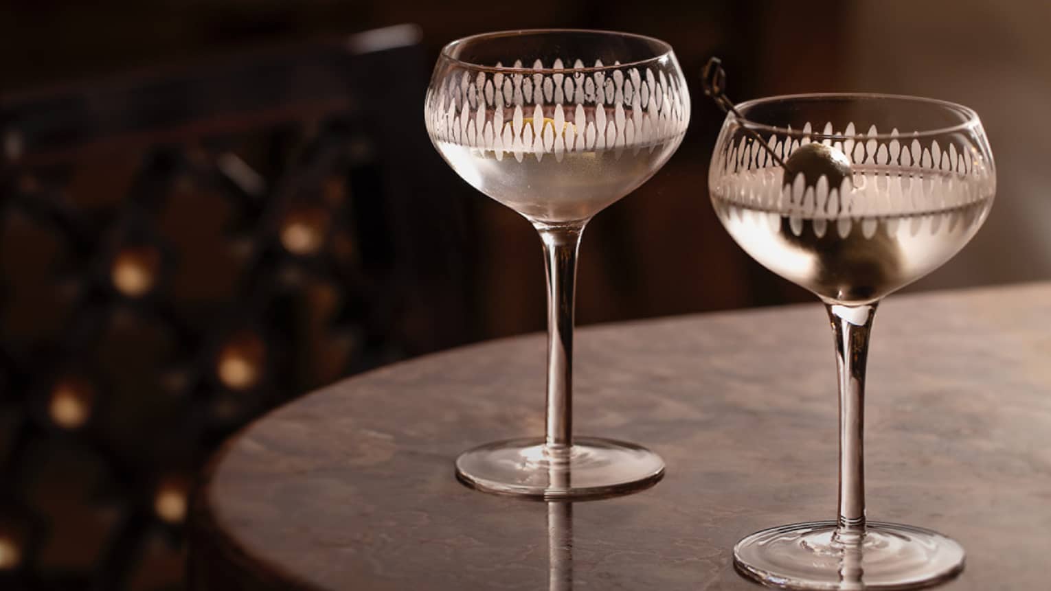,Two martinis sit on the edge of a black tabletop