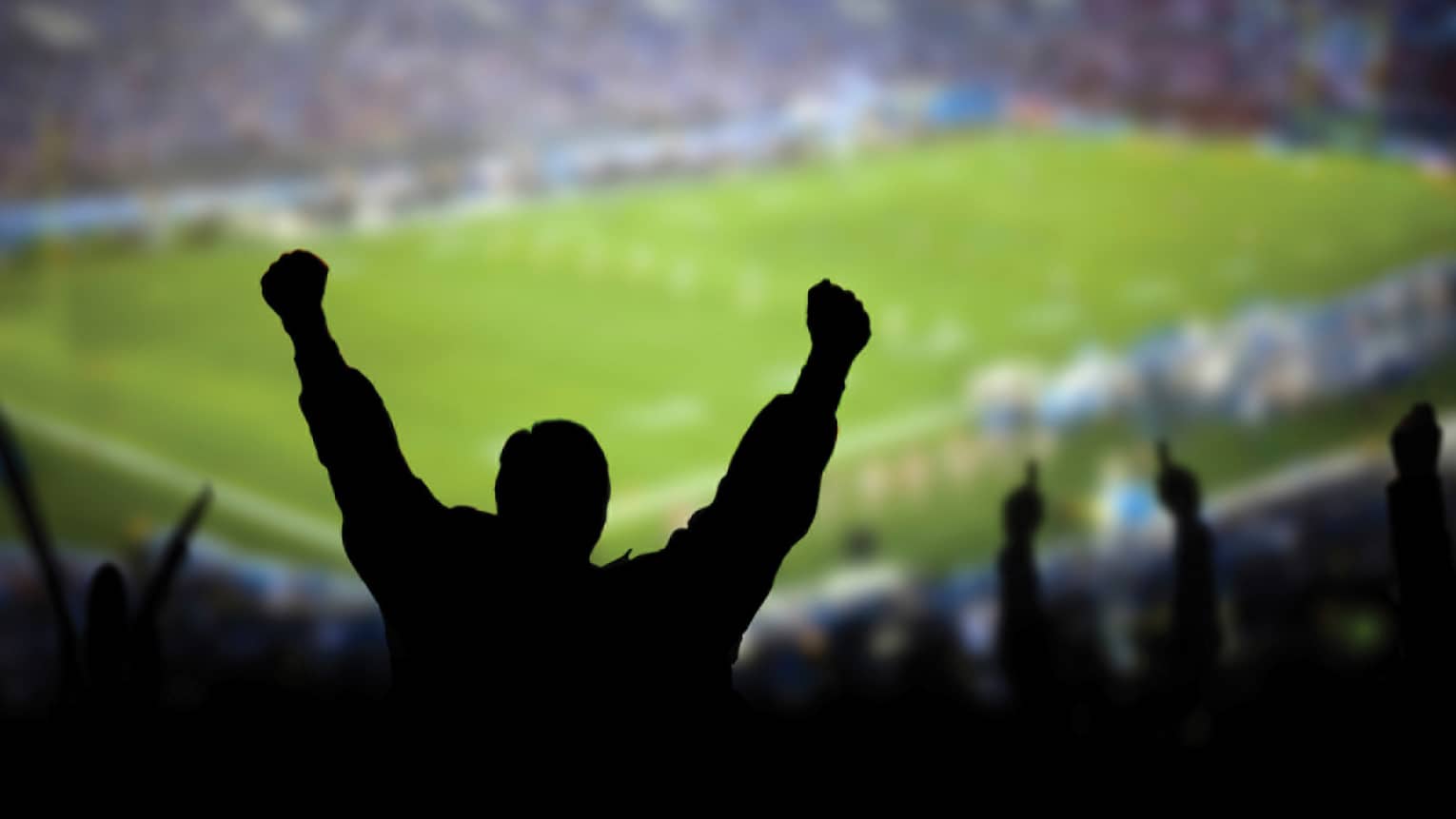 A silhouette of a person cheering at a football stadium.