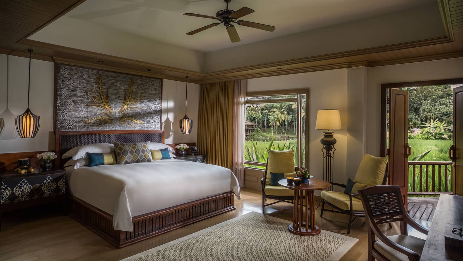 Rice Terrace Room bed with blue, gold accent pillows under painting, table by window with plantation view