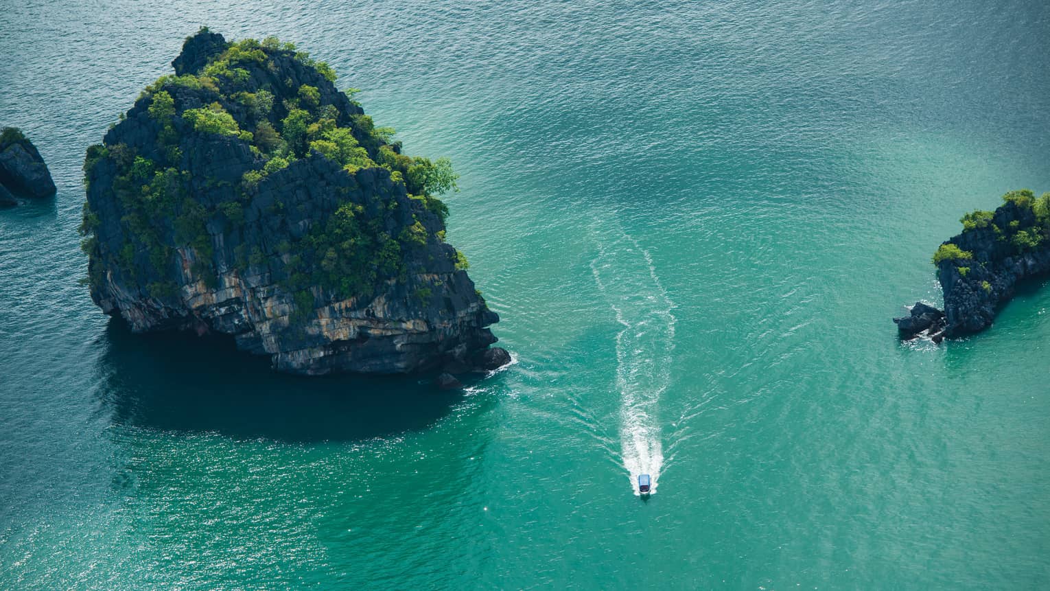 Ariel view of a boat driving through rock structures on emerald green water 