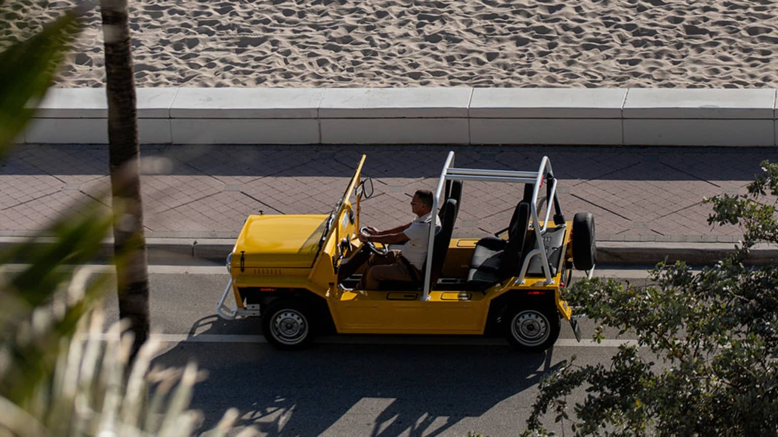 Guest driving a MOKE on the road beside the beach.