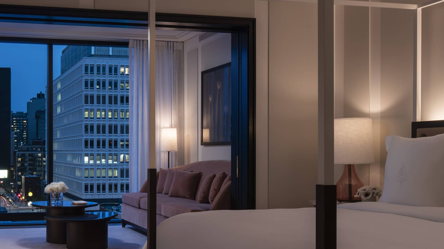 Presidential Suite dimly lit and with all-white modern four-poster bed and evening balcony view