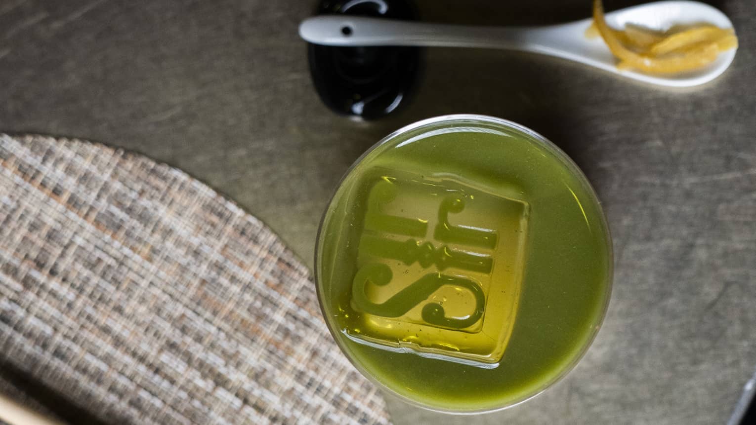 Green matcha cocktail with large square ice cube in the centre