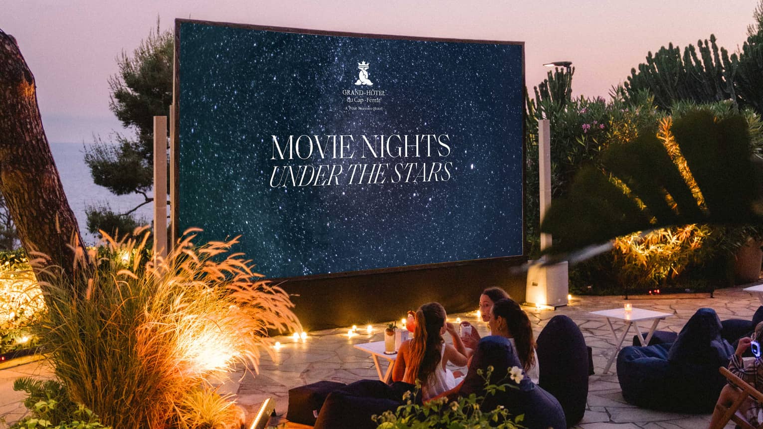 Families sit in front of a large outdoor movie screen