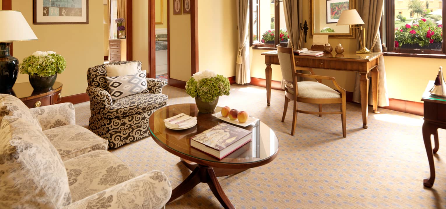 Four Seasons Executive Suite sunny living area, desk and chair in front of tall windows