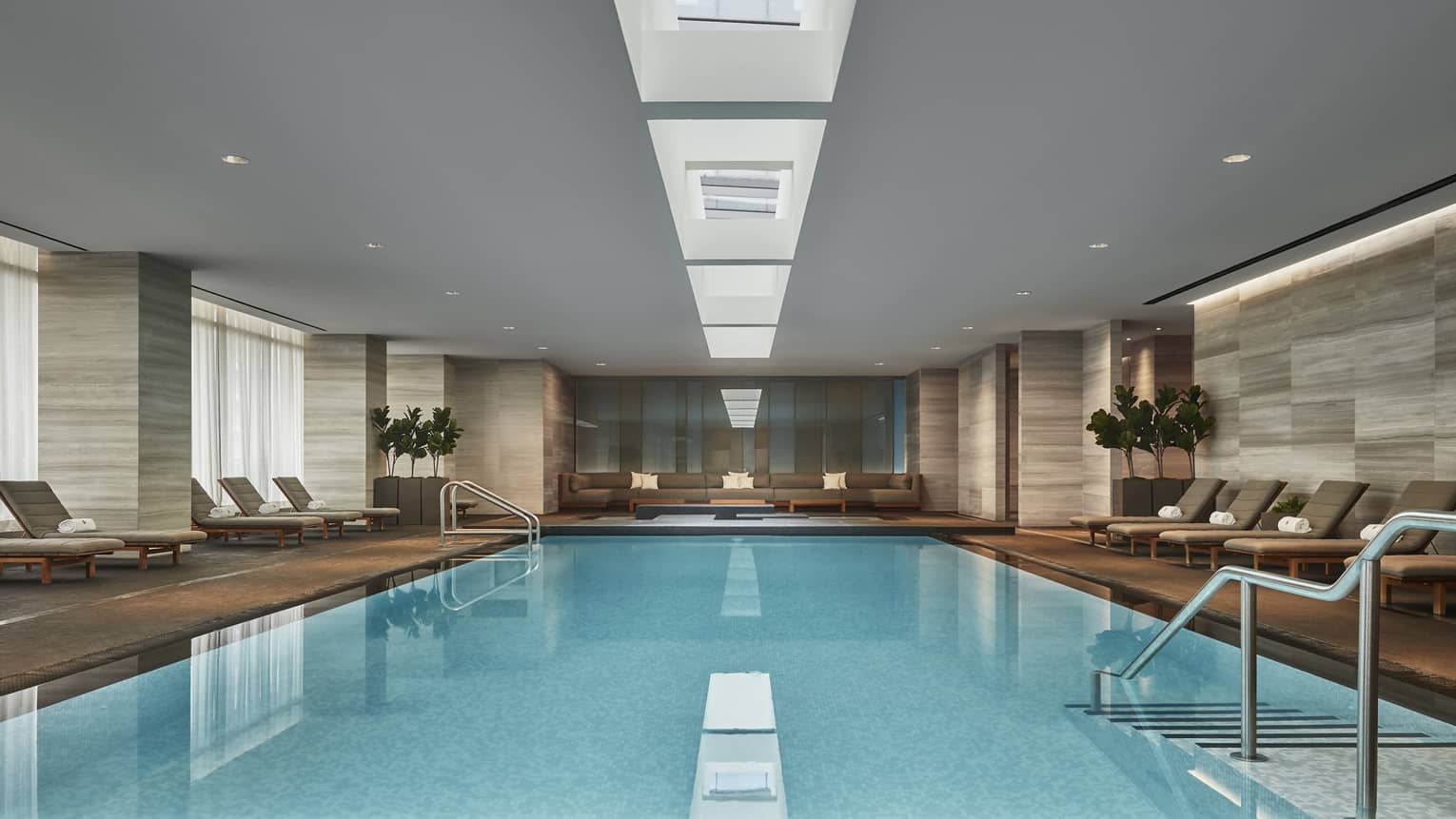 A long pool with a gentle sloping staircase that enters the water. Several lounge chairs surround the pool. 