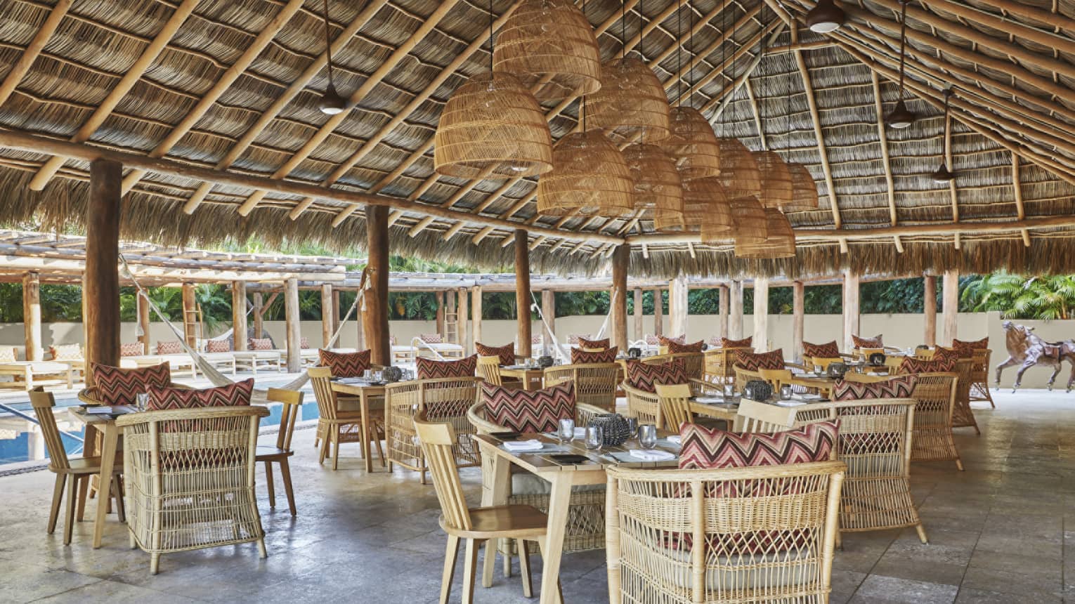Restaurant under thatched roof pavilion, with whicker chairs and hanging lights
