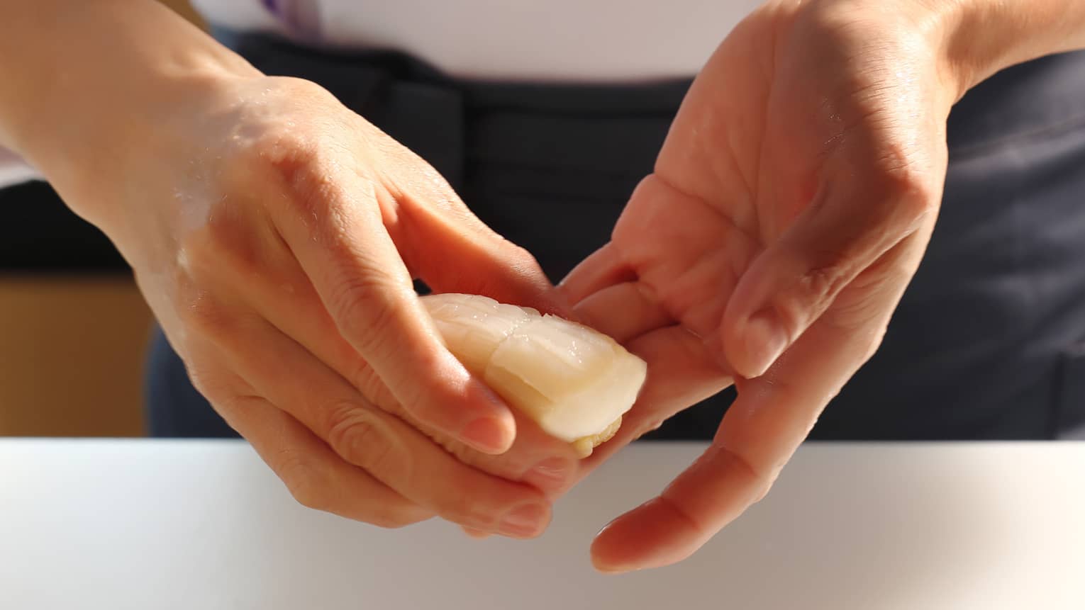 Extreme close-up of two hands holding a fresh piece of raw, pale-coloured seafood.