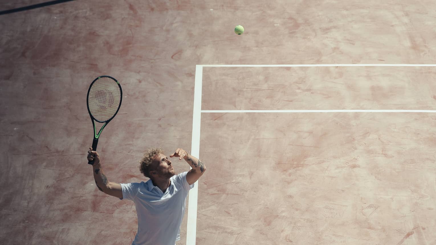 Man in white outfit playing tennis on reddish clay court