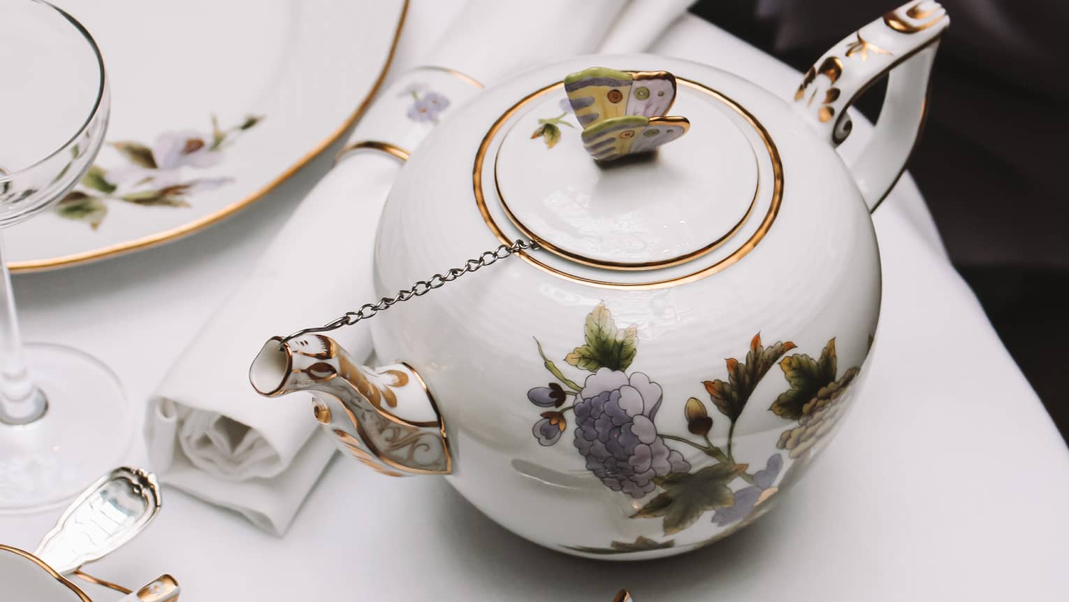 A white tea set with purple and yellow flowers on a white cloth table.