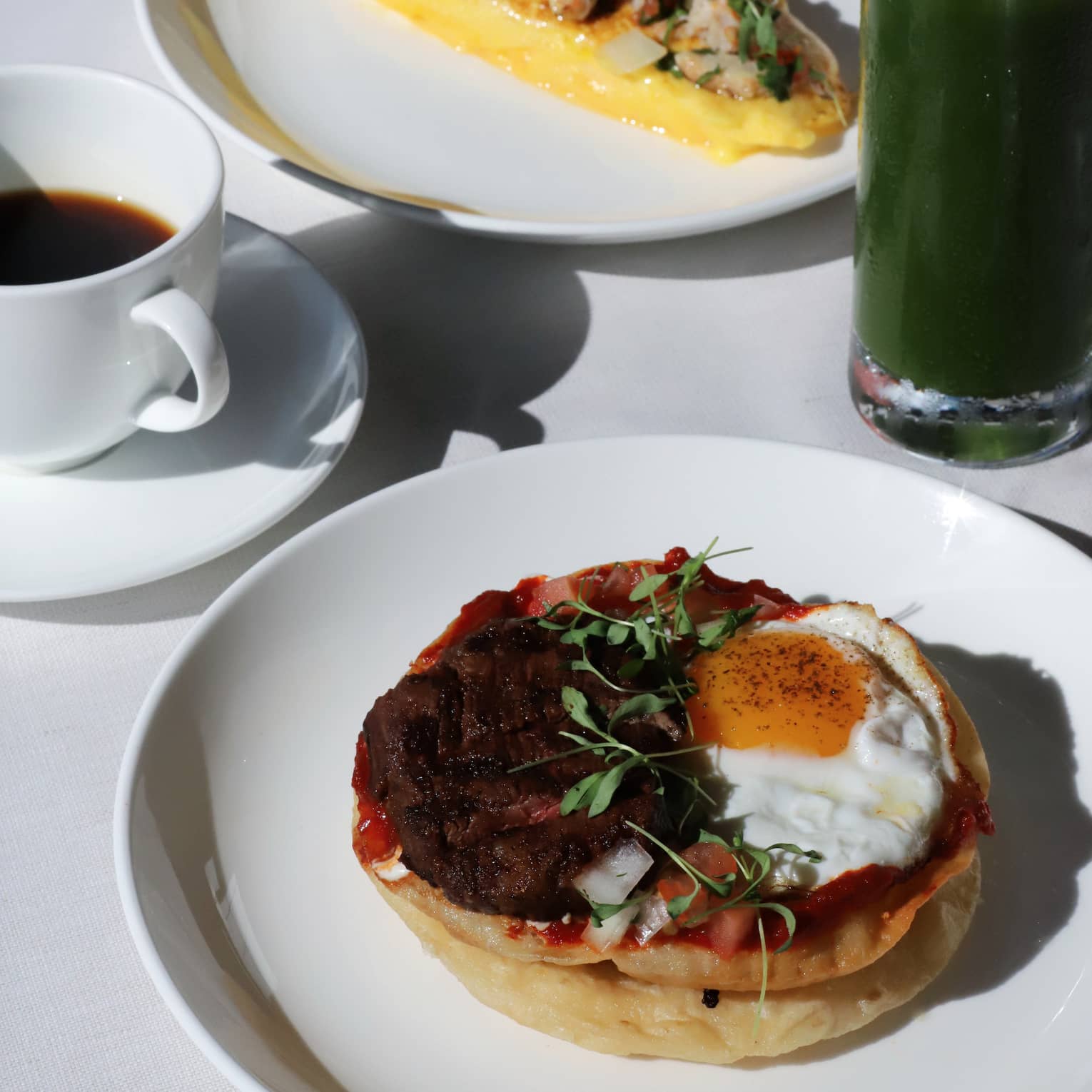 Close up of a table filled with breakfast dishes, green juice and coffee